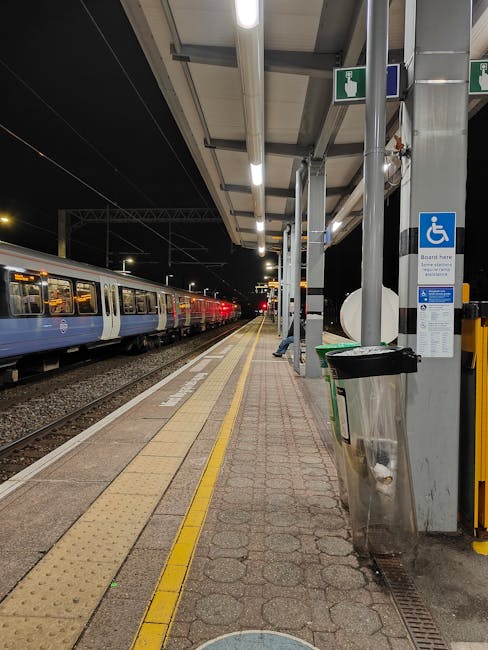 An underground station platform featuring a curved, white ceiling with bright linear lighting. The tiled walls display London Underground signage and various advertisements, including a sleep apnea pr